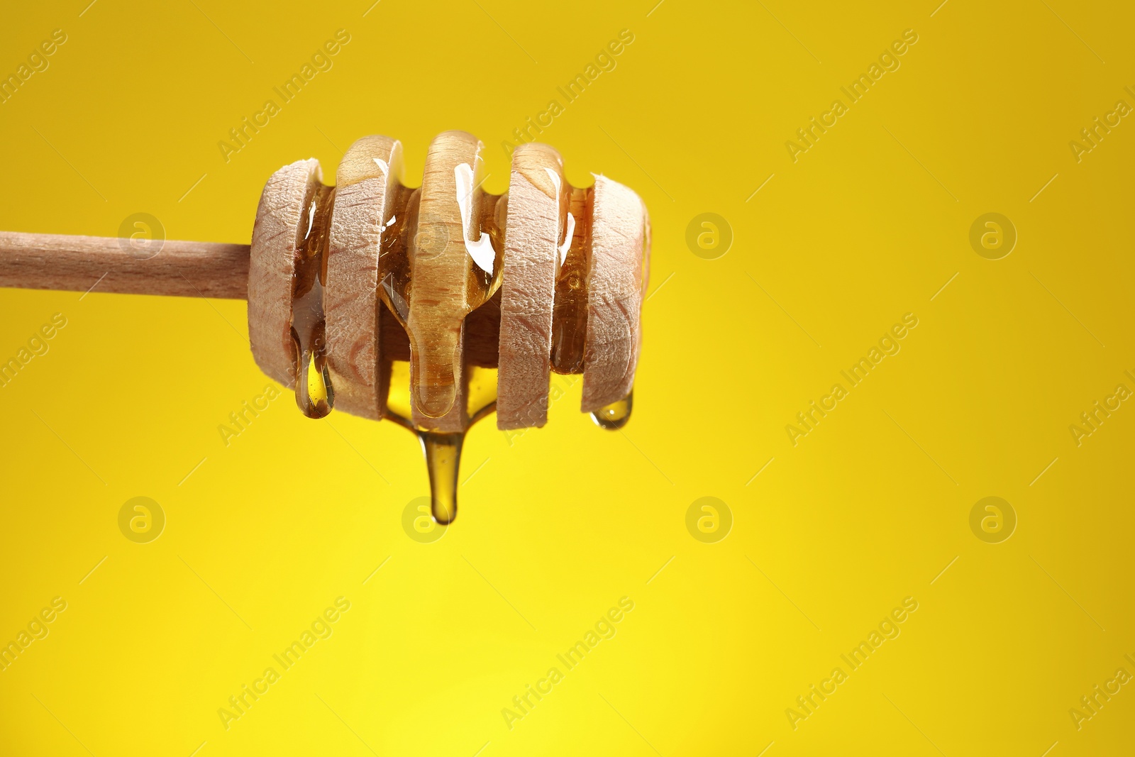 Photo of Delicious honey flowing down from dipper against yellow background, closeup. Space for text