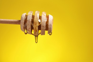 Delicious honey flowing down from dipper against yellow background, closeup. Space for text