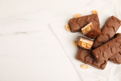 Photo of Chocolate bars with caramel, nuts and nougat on white marble table, flat lay. space for text