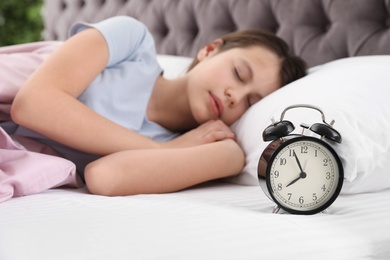 Photo of Beautiful little girl sleeping near alarm clock in bed, closeup