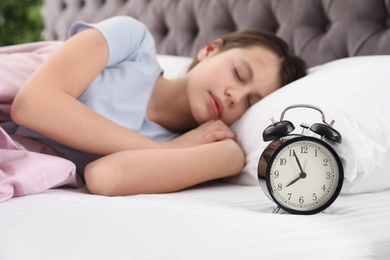 Beautiful little girl sleeping near alarm clock in bed, closeup