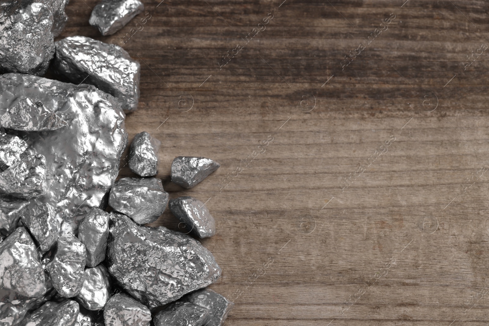 Photo of Pile of silver nuggets on wooden table, flat lay. Space for text