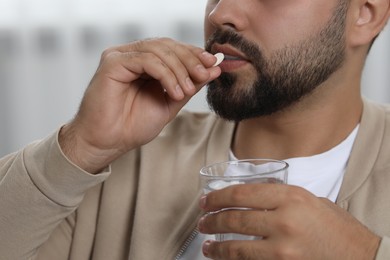 Photo of Man with glass of water taking antidepressant pill on blurred background, closeup