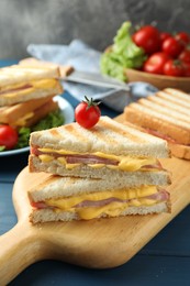 Tasty sandwiches with ham, melted cheese and tomato on blue wooden table