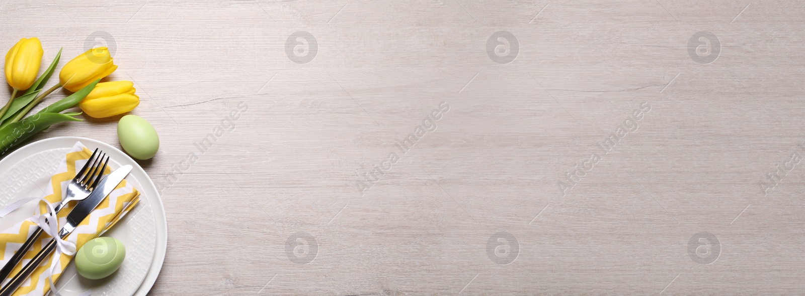 Image of Festive Easter table setting with eggs and flowers on light wooden background, flat lay. Space for text