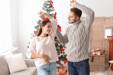Photo of Happy young couple dancing near Christmas tree at home