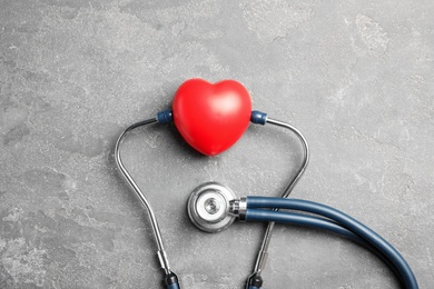 Photo of Stethoscope and red heart on gray background, top view. Cardiology concept