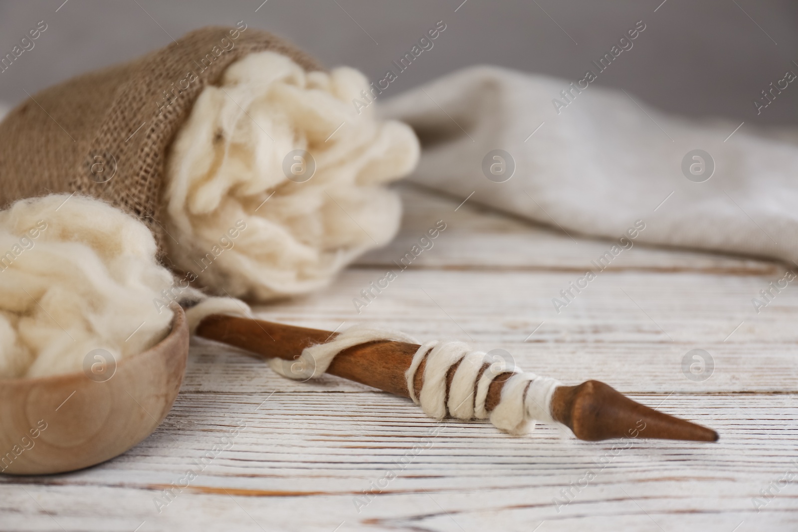 Photo of Soft white wool and spindle on wooden table. Space for text