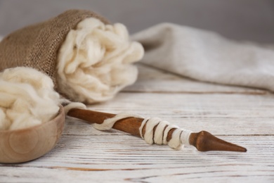 Soft white wool and spindle on wooden table. Space for text