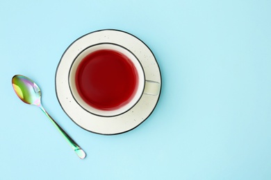 Photo of Cup of hibiscus tea with saucer and spoon on light blue background, flat lay. Space for text