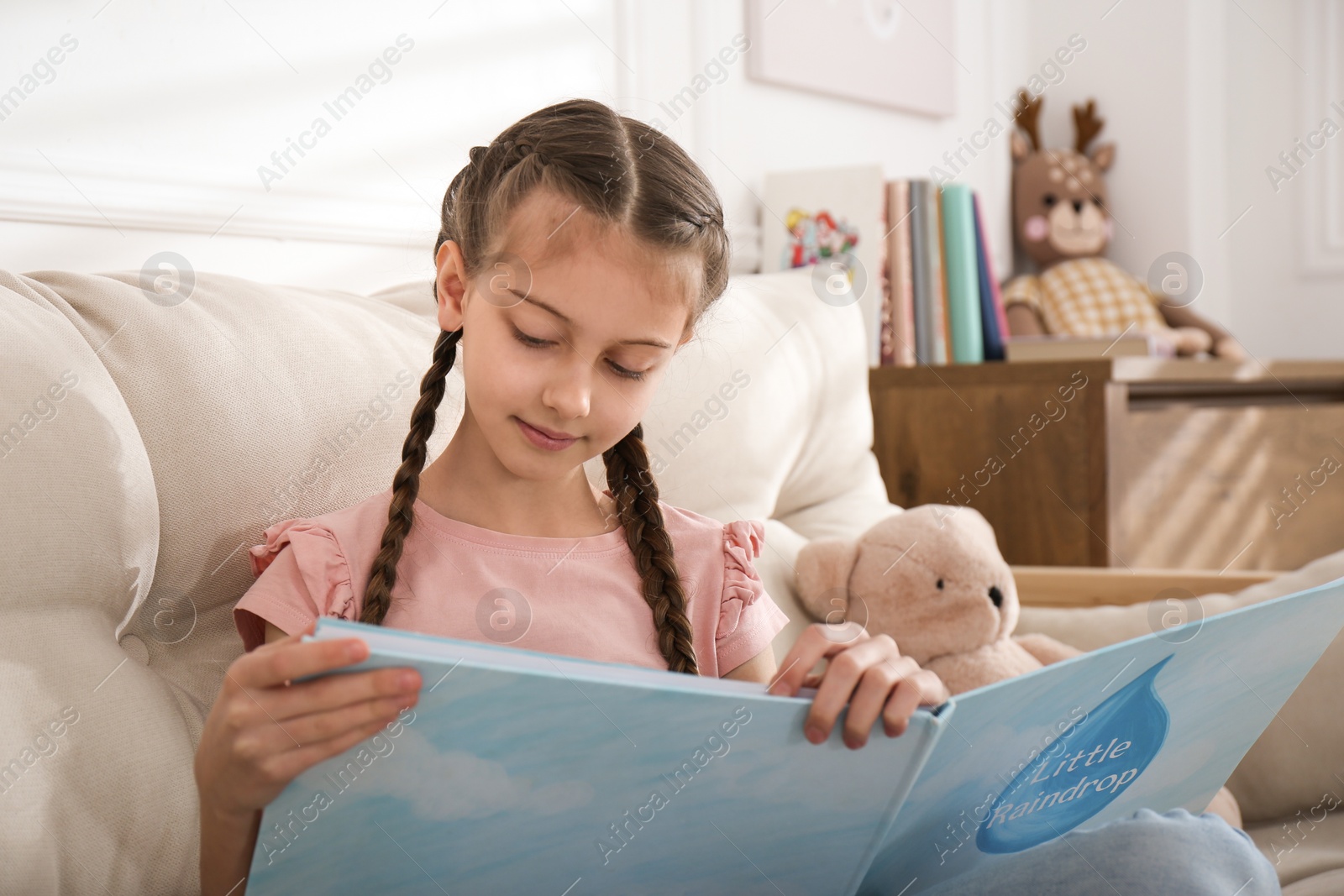 Photo of Cute little girl reading book on sofa at home