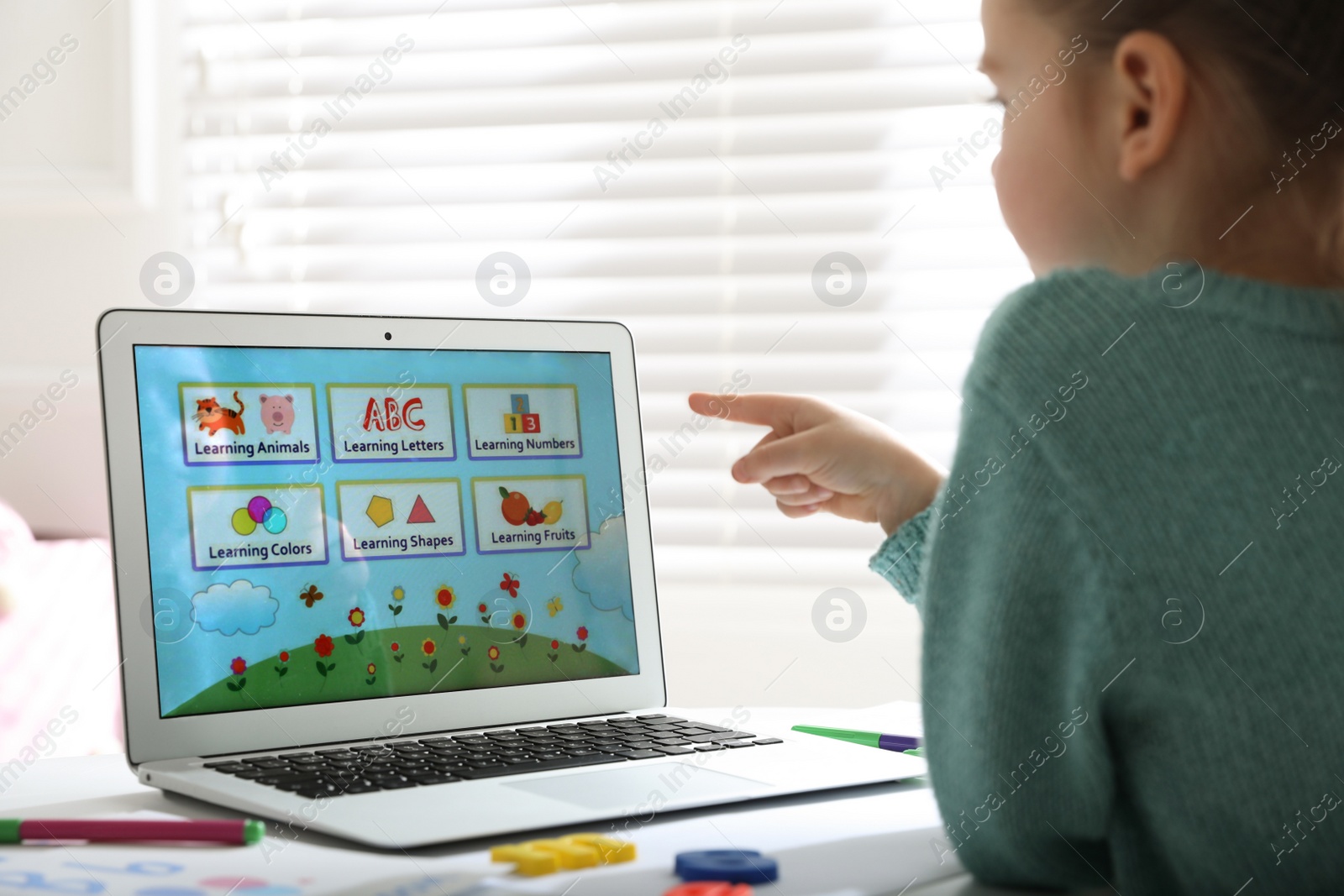 Photo of Little girl learning English indoors at online lesson, closeup