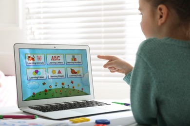 Photo of Little girl learning English indoors at online lesson, closeup