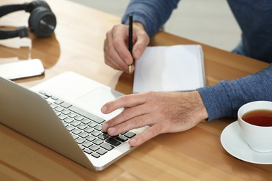 Man with laptop and notebook learning at wooden table indoors, closeup