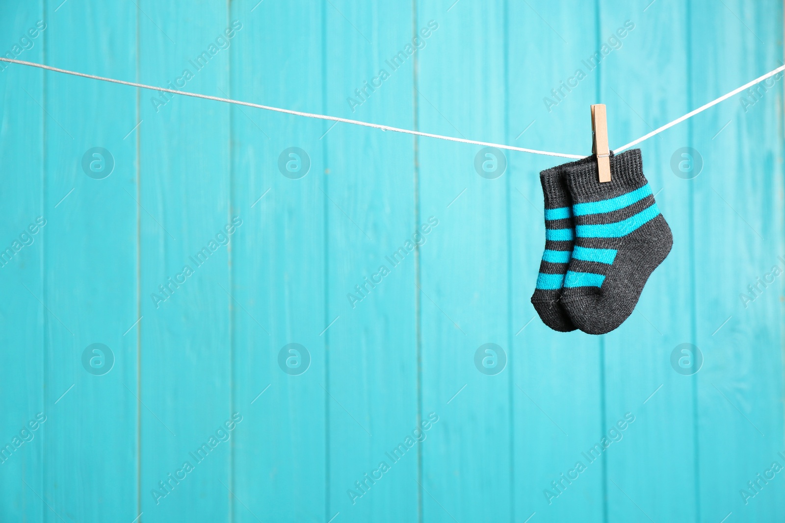 Photo of Baby socks on laundry line against color wooden background, space for text. Child accessories