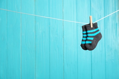 Baby socks on laundry line against color wooden background, space for text. Child accessories