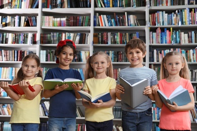 Group of little children reading books near shelves in library