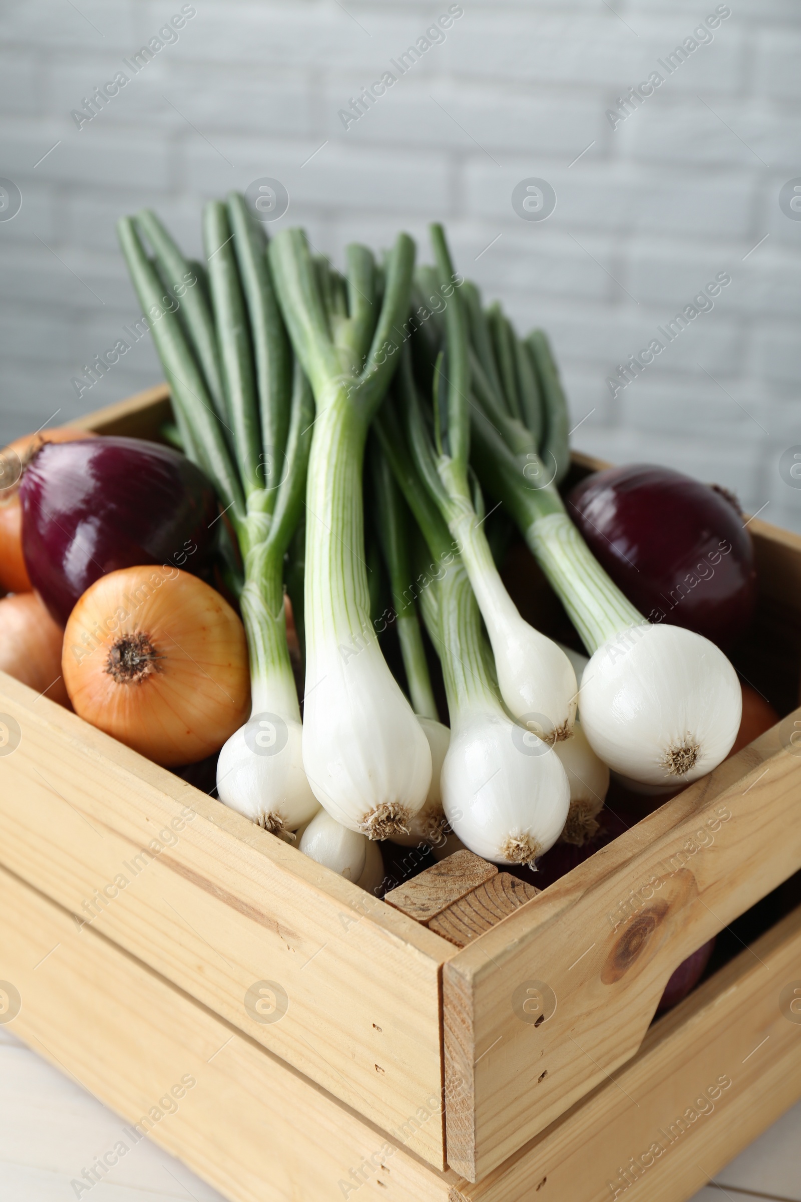 Photo of Crate with different kinds of onions on table, closeup