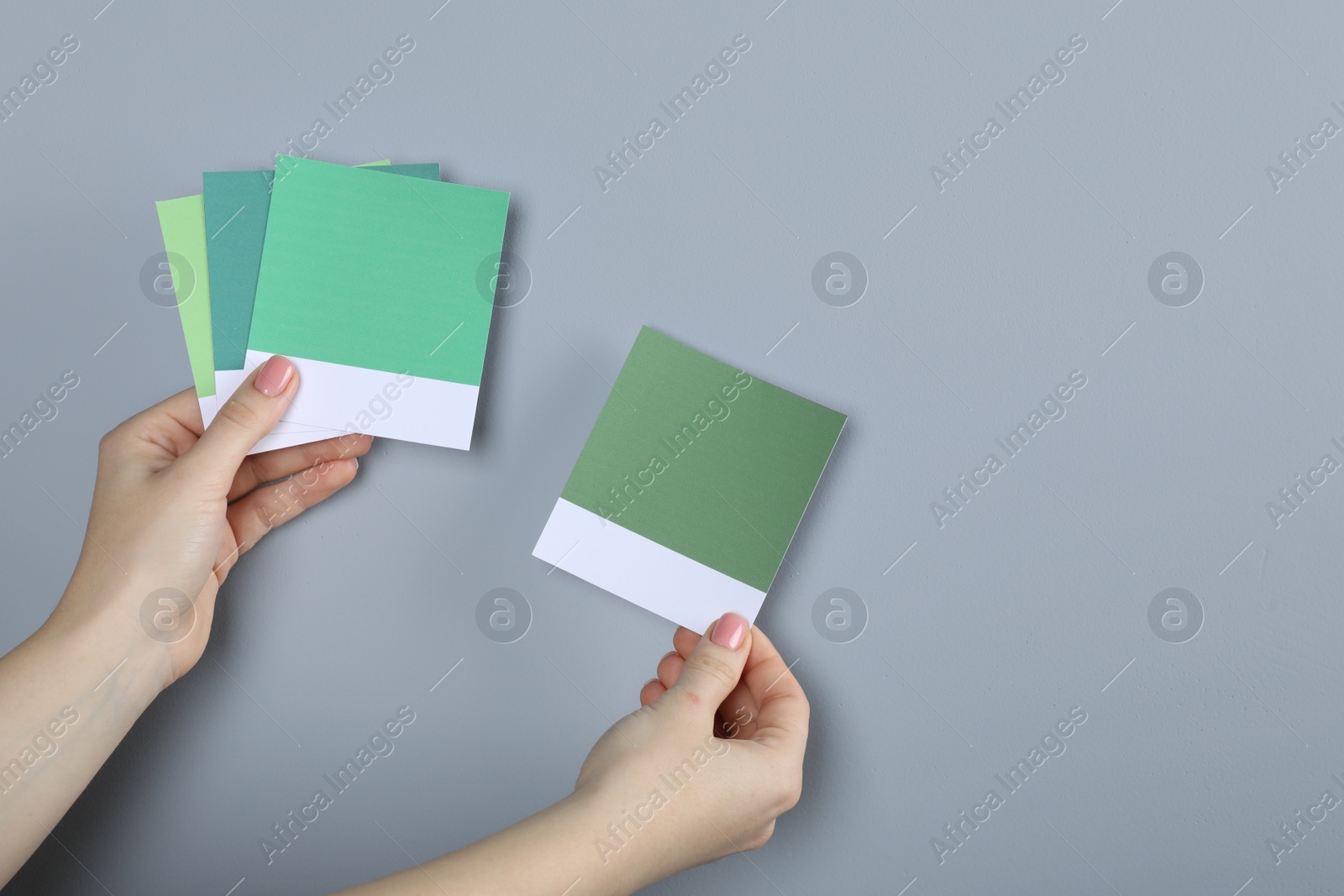 Photo of Woman with color sample cards choosing paint shade near grey wall, closeup. Interior design