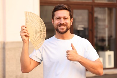 Happy man holding hand fan on city street