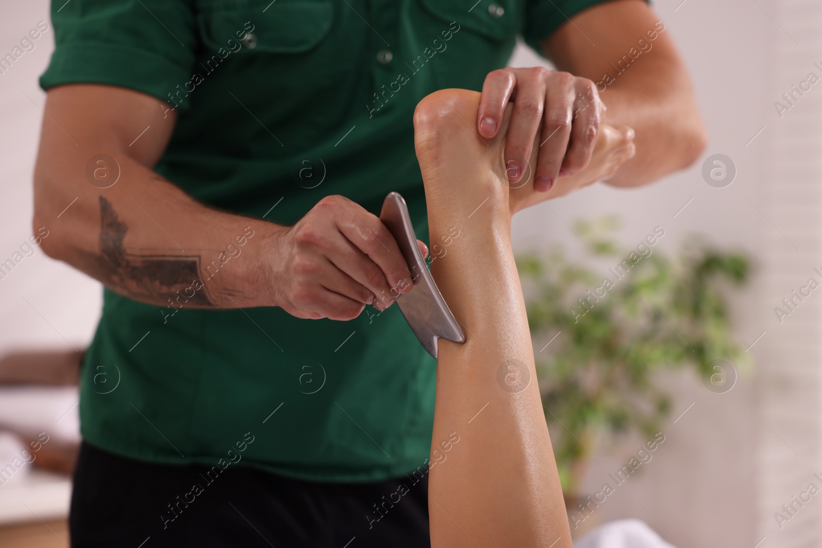 Photo of Woman receiving professional leg massage with gua sha indoors, closeup