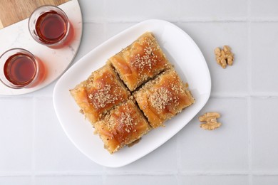 Photo of Eastern sweets. Pieces of tasty baklava, walnuts and tea on white tiled table, flat lay