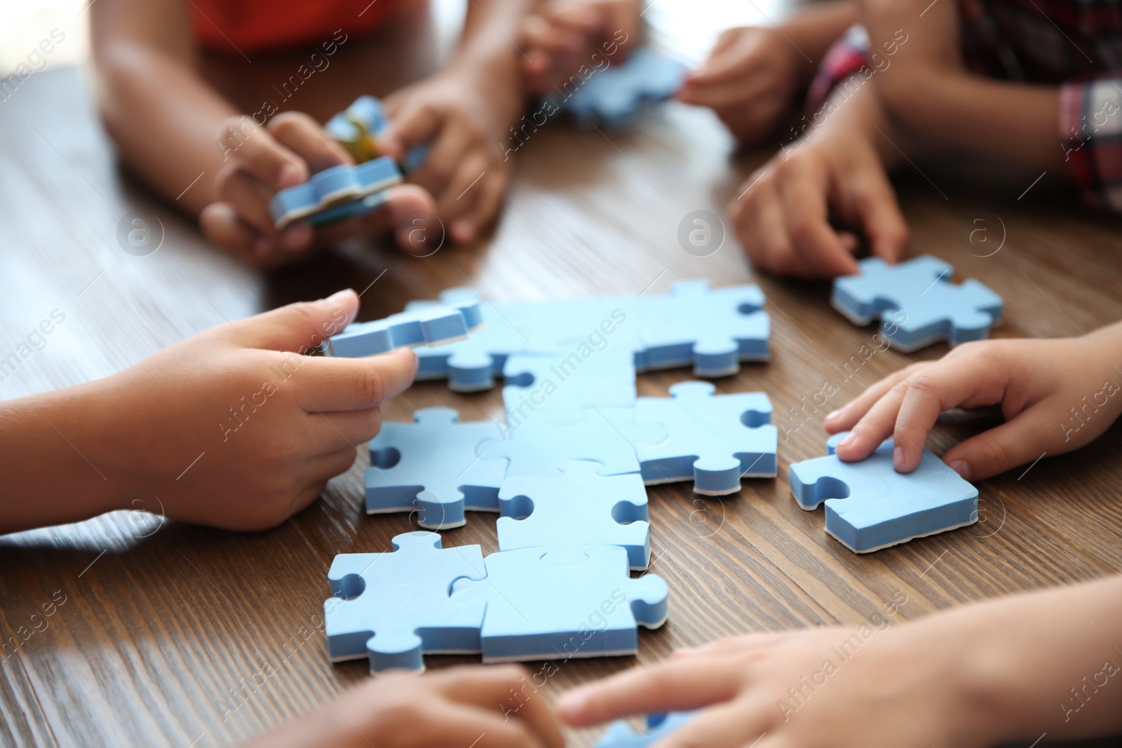 Photo of Little children playing with puzzle at table, focus on hands. Unity concept
