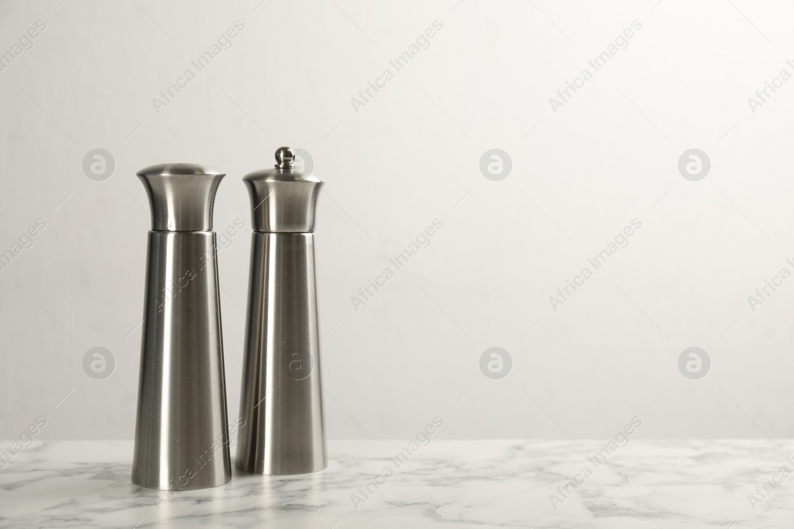 Photo of Stainless salt and pepper shakers on marble table against white background. Space for text