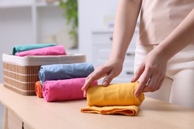 Woman rolling shirt at table in room, closeup. Organizing clothes