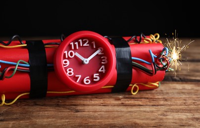 Photo of Dynamite time bomb on wooden table against black background, closeup