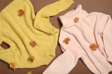 Photo of Warm sweaters and dry leaves on brown background, flat lay. Autumn season