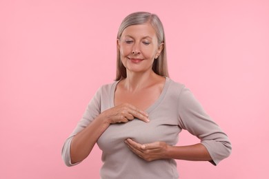 Photo of Beautiful senior woman doing breast self-examination on pink background