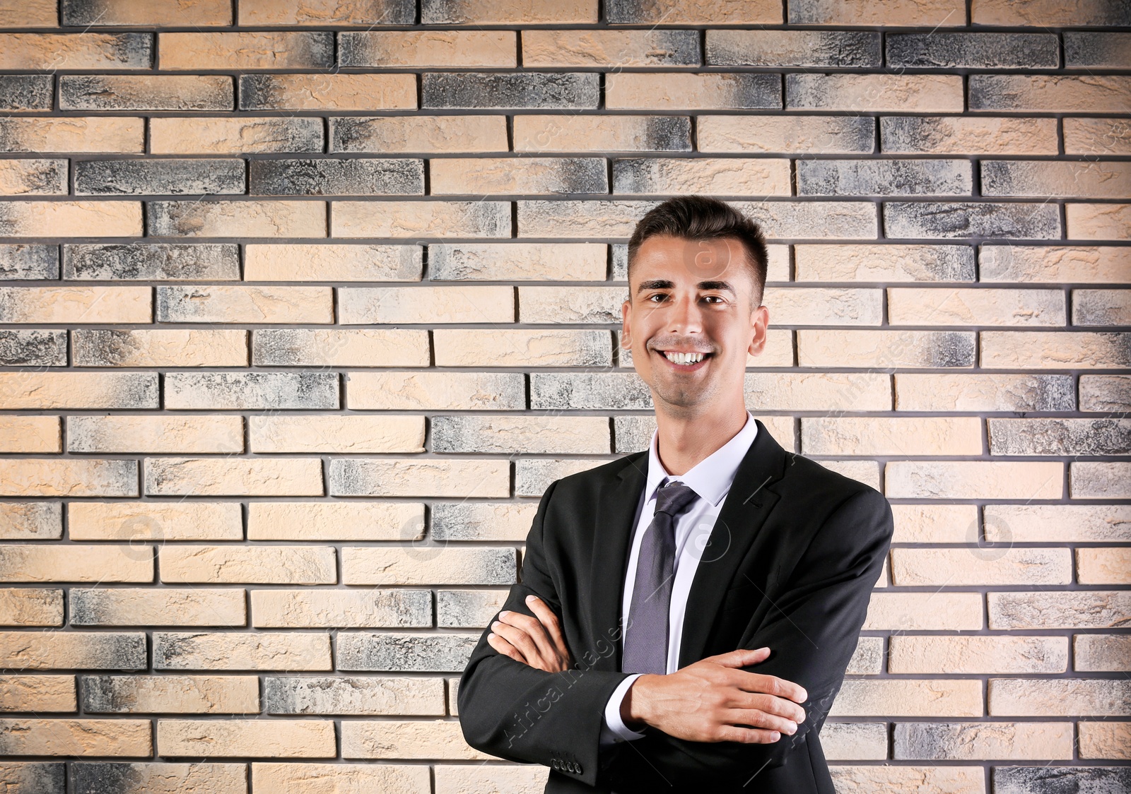 Photo of Handsome young man in suit near brick wall background