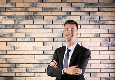 Handsome young man in suit near brick wall background