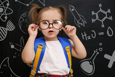 Image of Cute little child wearing glasses near chalkboard with different images