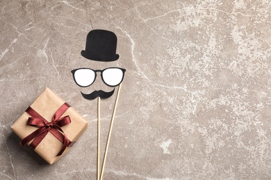 Gift box, paper glasses, hat and moustache on grey background, top view