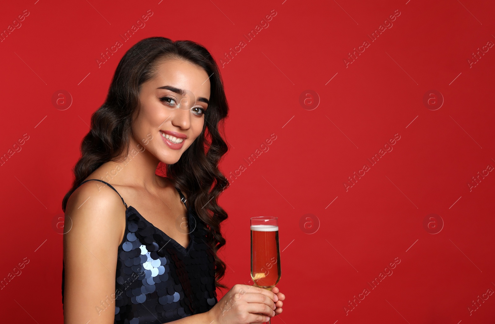 Photo of Beautiful young woman in elegant dress holding glass of champagne on red background. Christmas party