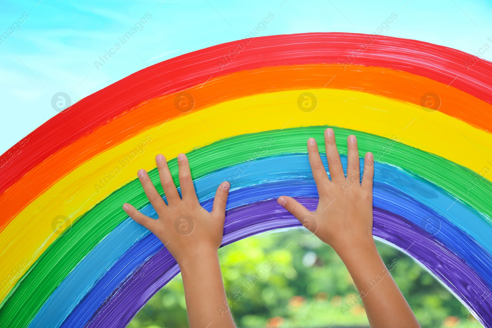 Photo of Child touching picture of rainbow on window, closeup. Stay at home concept