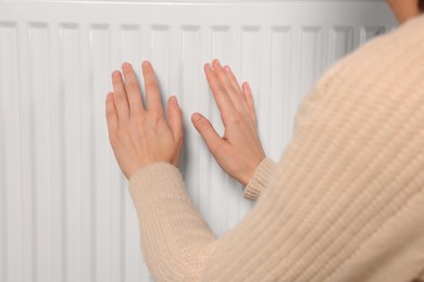 Woman warming hands on white heating radiator, closeup