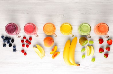 Many different tasty smoothies and ingredients on white wooden table, flat lay