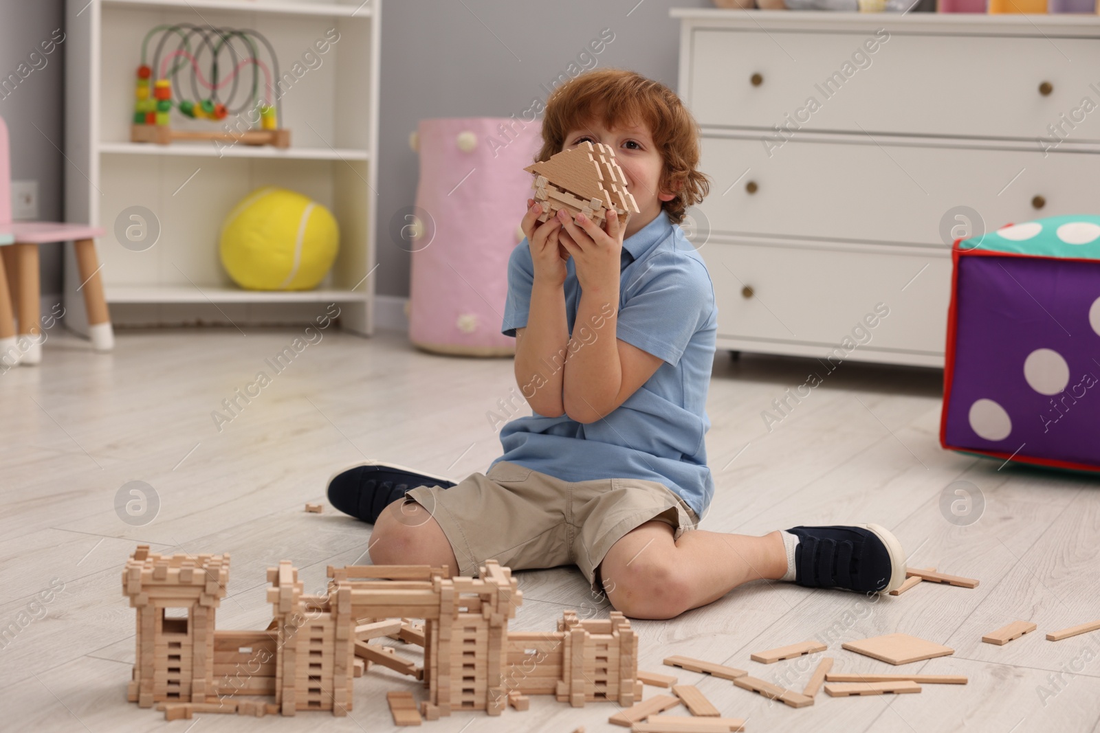 Photo of Little boy playing with wooden construction set on floor in room. Child's toy