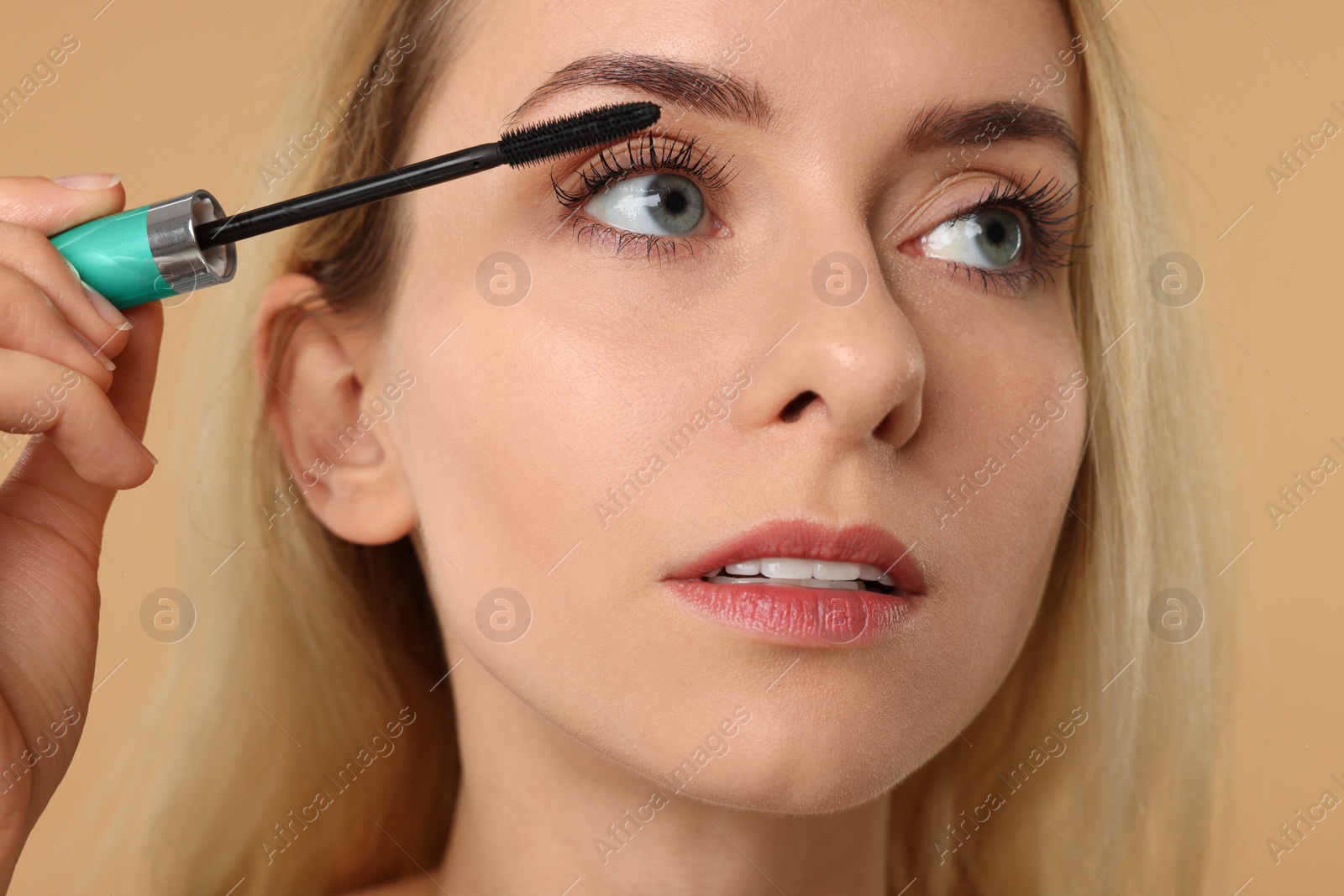 Photo of Beautiful woman applying mascara on beige background, closeup