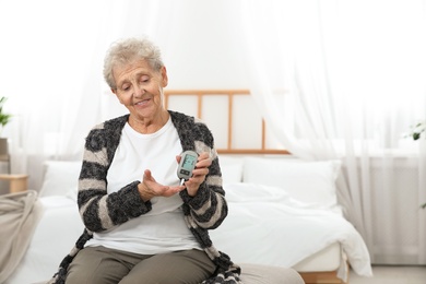 Photo of Senior woman using digital glucometer at home. Diabetes control