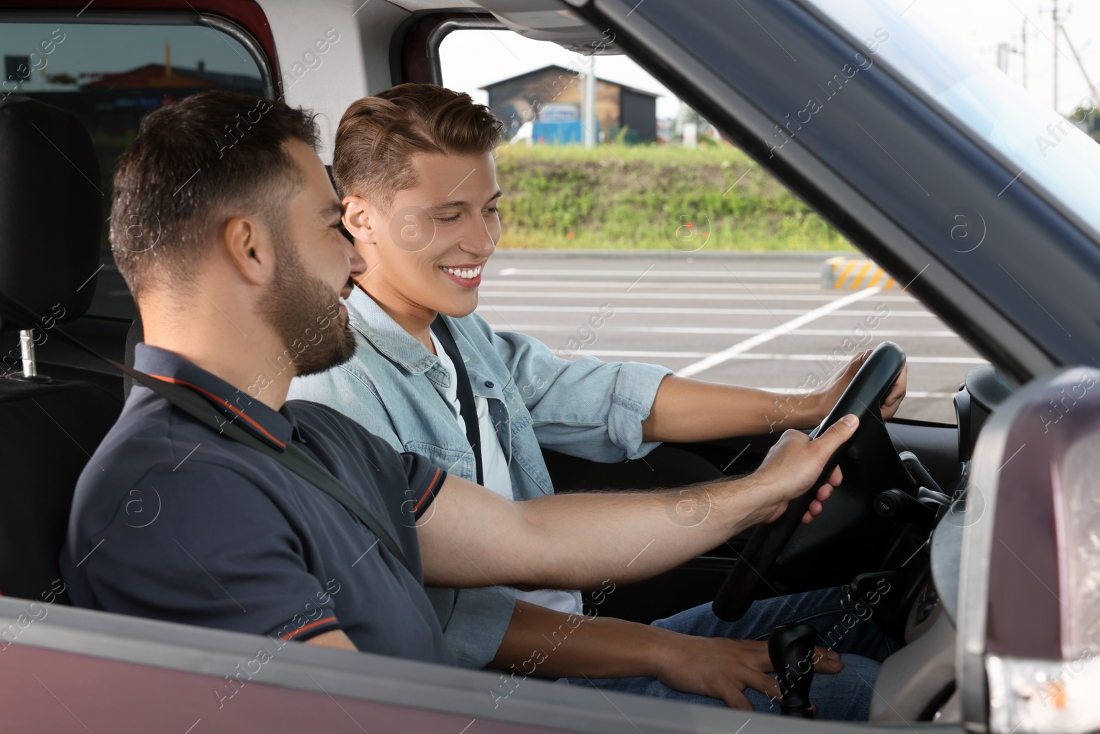 Photo of Driving school. Happy student during lesson with driving instructor in car at parking lot