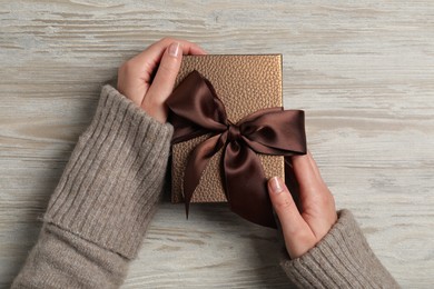 Woman holding gift box at wooden background, top view