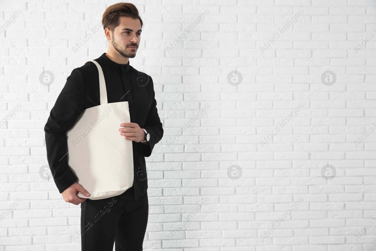 Photo of Young man holding textile bag against brick wall.  Mockup for design