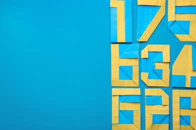 Photo of Different numbers made of paper on light blue background, flat lay. Space for text