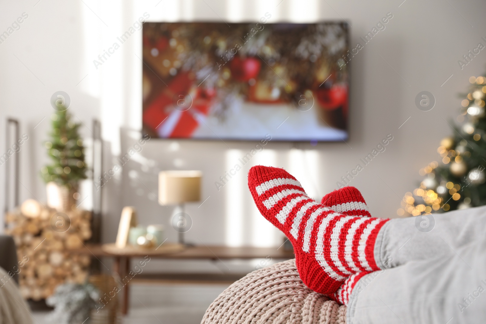 Photo of Woman wearing knitted socks in room decorated for Christmas, closeup