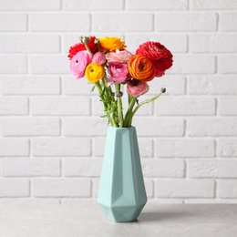 Photo of Beautiful fresh ranunculus flowers in vase on white table near brick wall