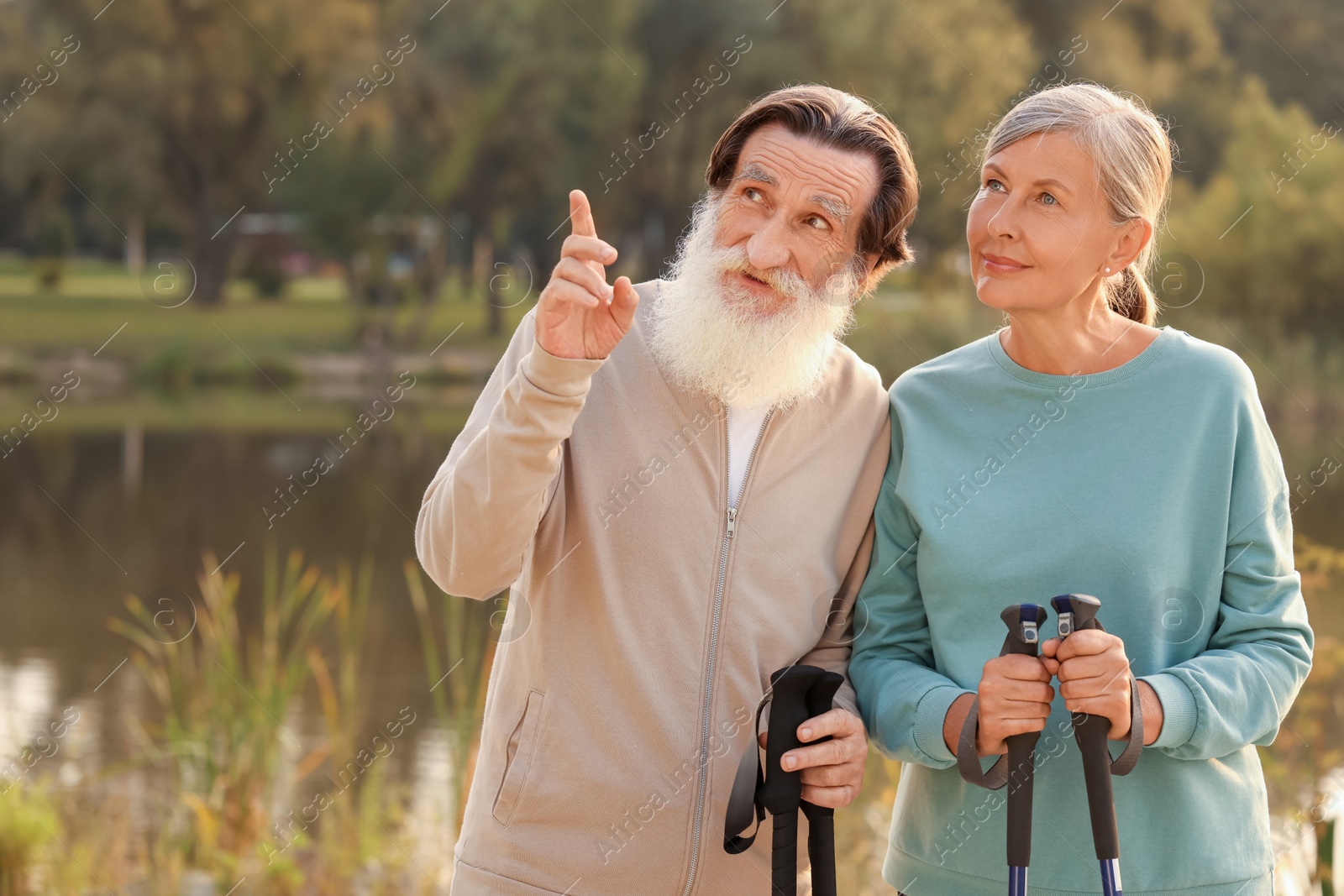 Photo of Senior man and woman with Nordic walking poles outdoors, space for text